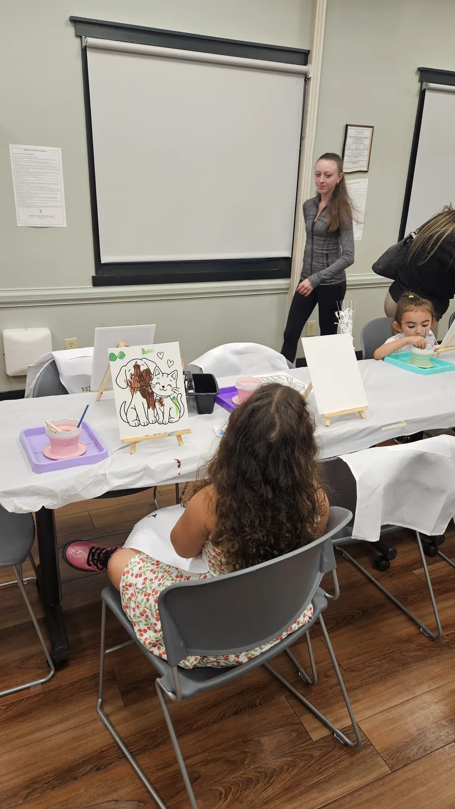 Child painting at a STEAM Sprouts activity table while an instructor stands nearby