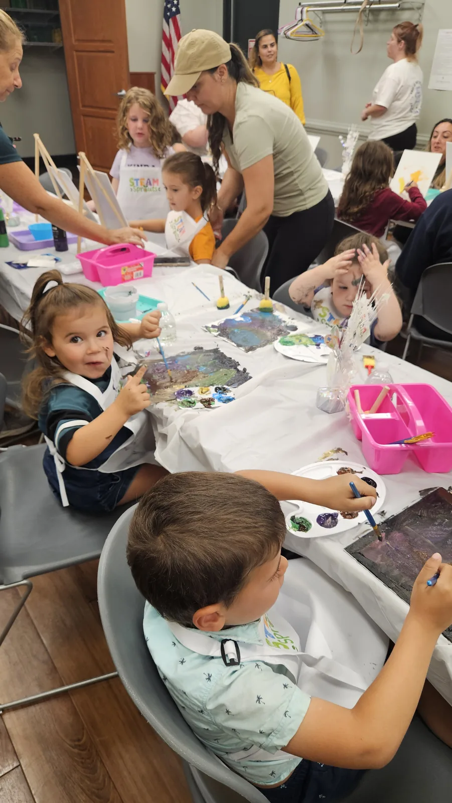Child and adults creating together at a busy STEAM Sprouts activity table