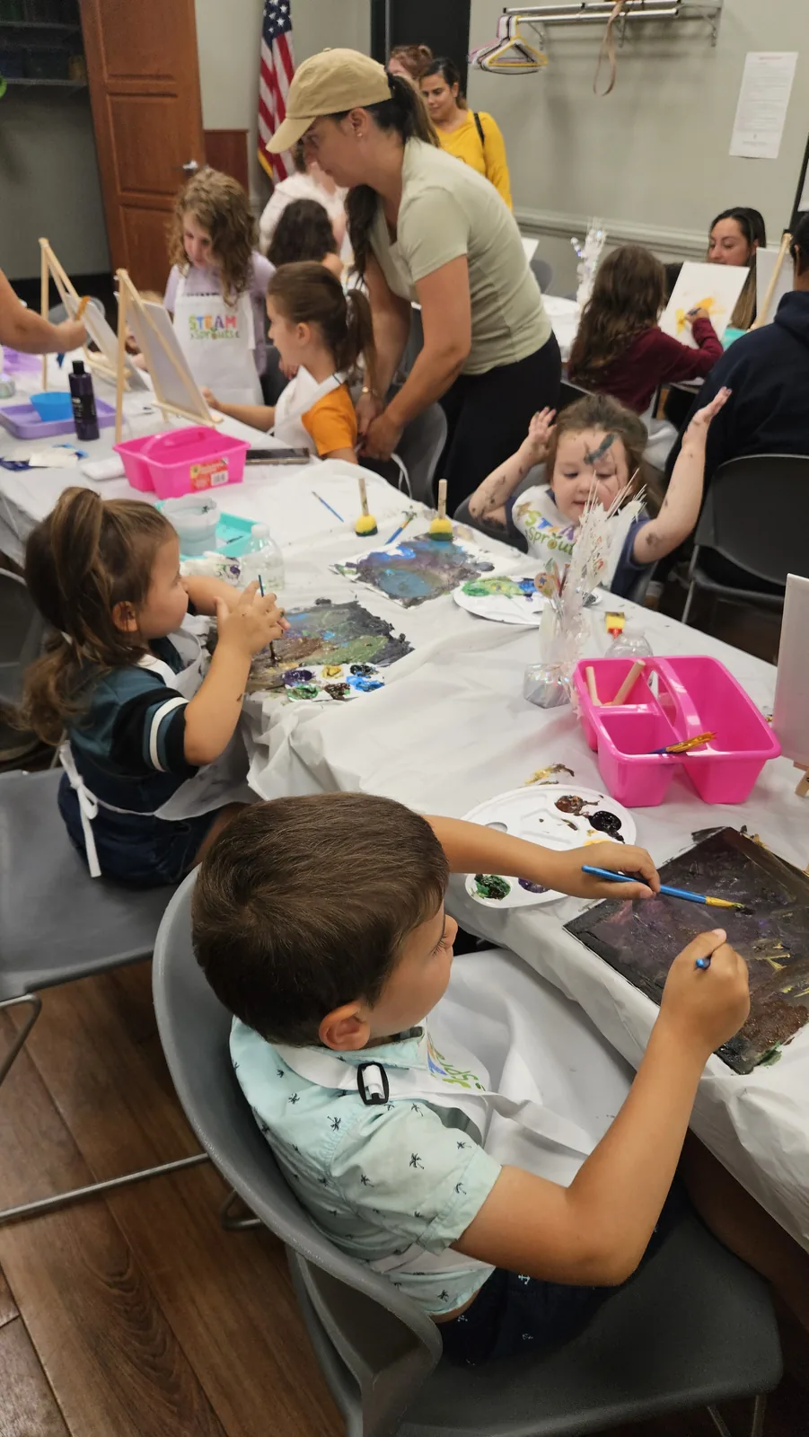 Three children seated beneath a STEAM Sprouts sign in a community event space
