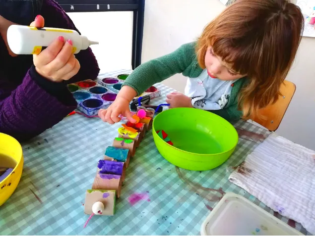 Child and grown-up assembling and painting a paper-tube creature craft at a craft table