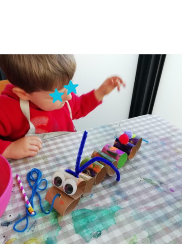 Young child making a cardboard-tube wiggly caterpillar craft at a STEAM Sprouts activity table